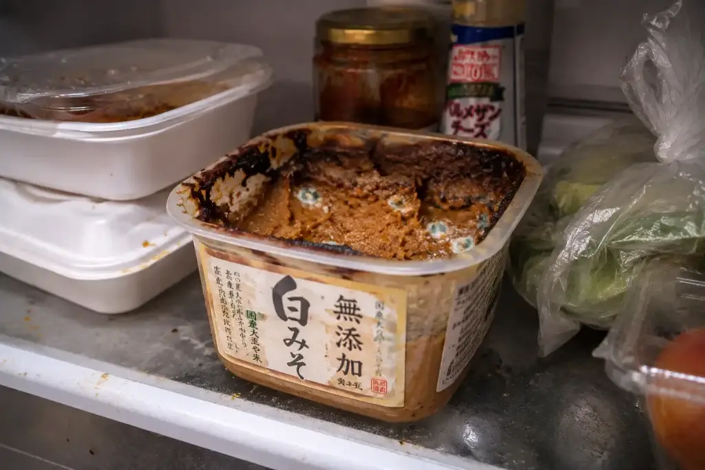 a cluttered refrigerator shelf with an open miso container
